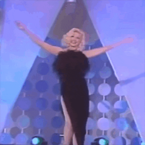 a woman in a black dress with her arms outstretched on a stage