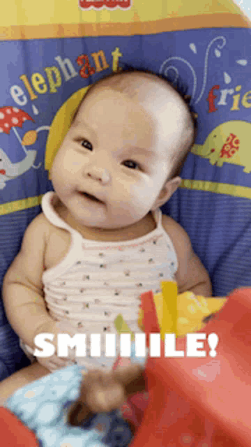 a baby is sitting in a high chair with an elephant blanket behind him