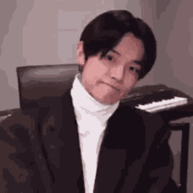 a young man in a suit and white turtleneck is sitting in front of a piano .