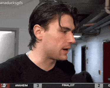 a man in a black shirt is talking into a microphone in front of a scoreboard that says anaheim