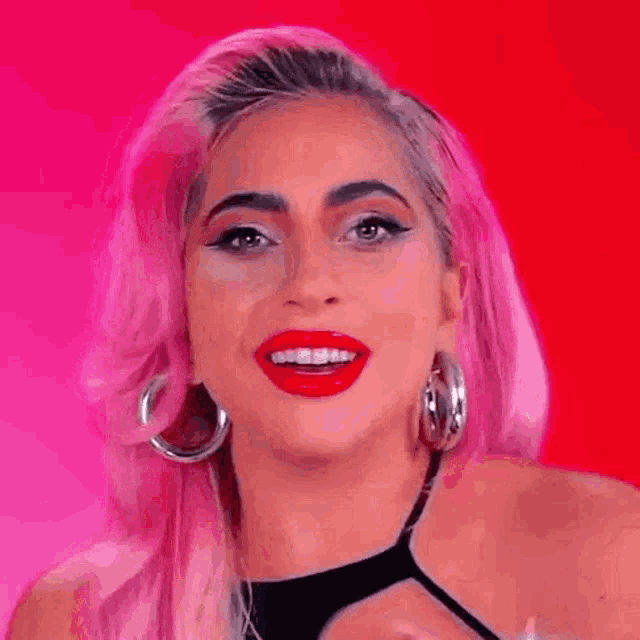 a close up of a woman with pink hair and red lips wearing hoop earrings .