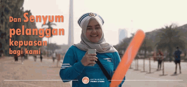 a woman wearing a hijab and a sailor hat is smiling while holding a frisbee and a cell phone