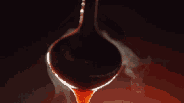 a red liquid is being poured from a ladle into a cup