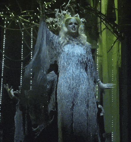 a woman in a blue dress with a crown on her head stands in a dark room