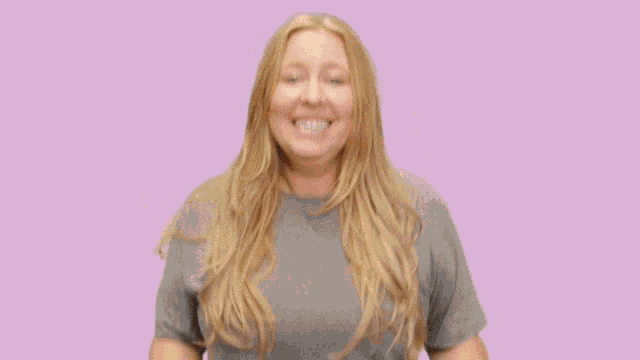 a woman wearing a grey t-shirt is smiling with her hands outstretched