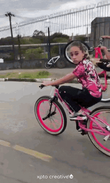 a girl in a pink shirt is riding a pink bicycle on a street