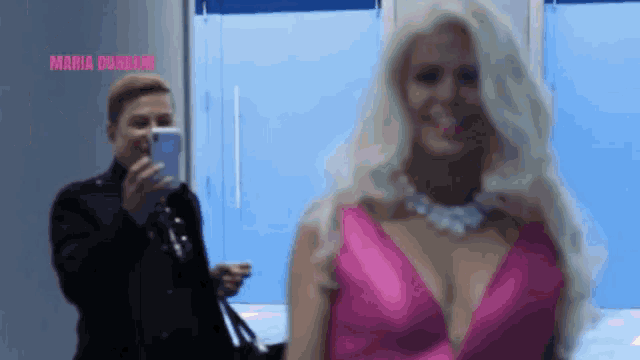 a woman in a pink dress is being photographed by a man in a black shirt .