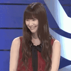 a woman with long hair is smiling and wearing a red shirt