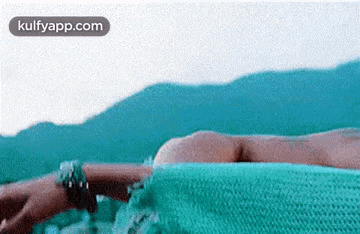 a woman is laying on a green blanket on a beach .