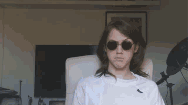 a young man wearing sunglasses and a white shirt is sitting in a chair