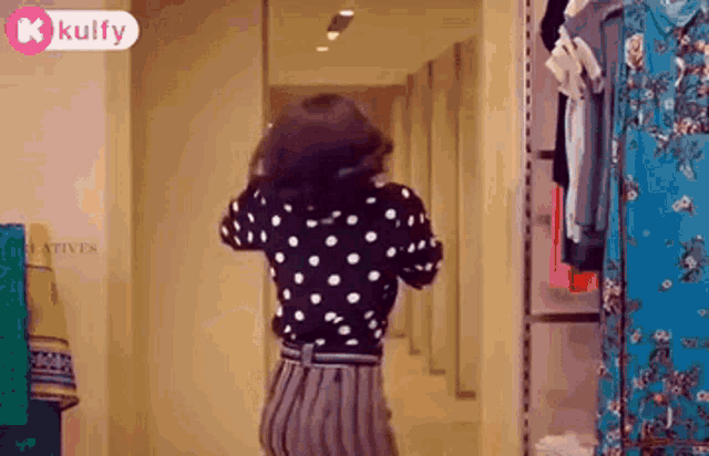 a woman in a polka dot shirt and striped pants is dancing in a dressing room .