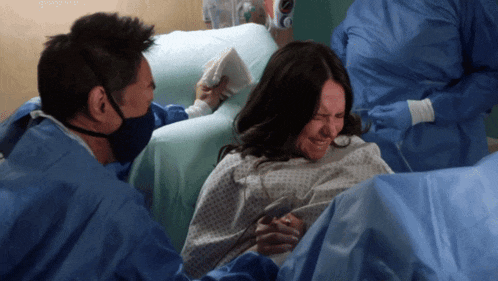 a woman in a hospital gown is crying while a man holds her hand