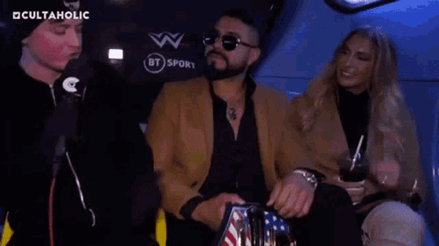 a man is holding a wrestling belt in front of a microphone while sitting next to a woman .