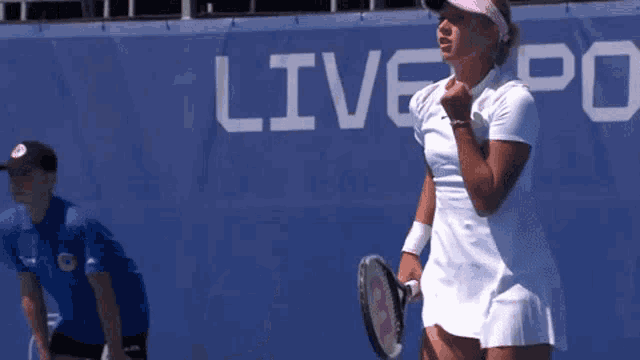a woman in a white dress is holding a tennis racquet in front of a banner that says liv spo