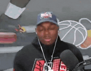 a man wearing a rockets hat is talking into a microphone while wearing headphones .