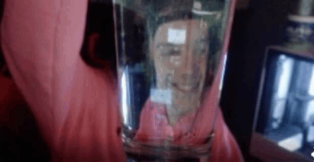 a person is holding a glass of water with a reflection of a woman 's face in it .