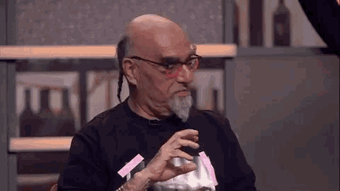 a bald man with glasses and a beard is sitting in front of a microphone .
