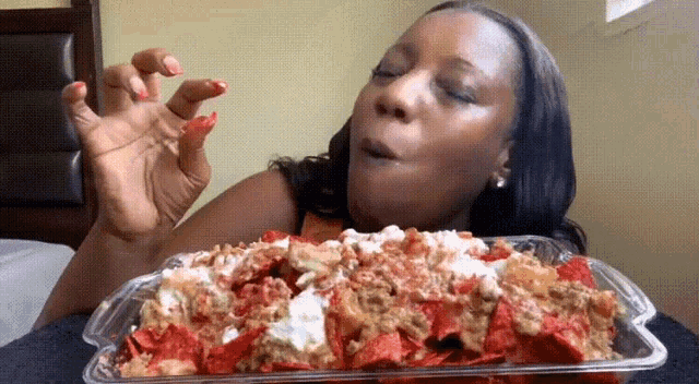 a woman is sitting at a table eating a casserole dish of nachos