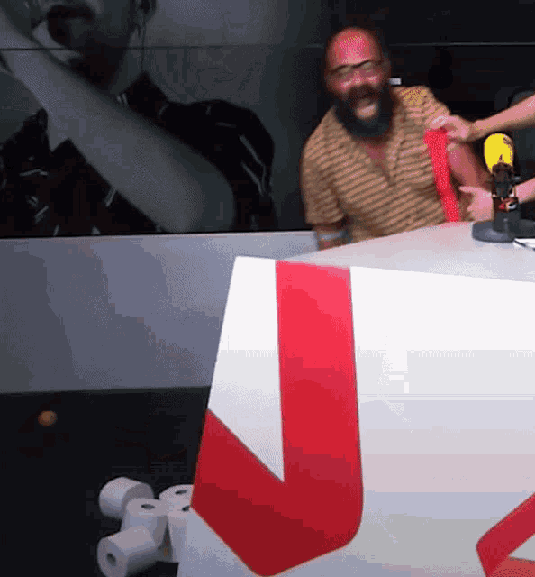 a man with a beard is sitting at a desk with a microphone and a bunch of toilet paper