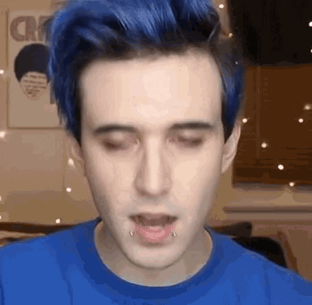 a man with blue hair is wearing a blue shirt and has piercings in his mouth .