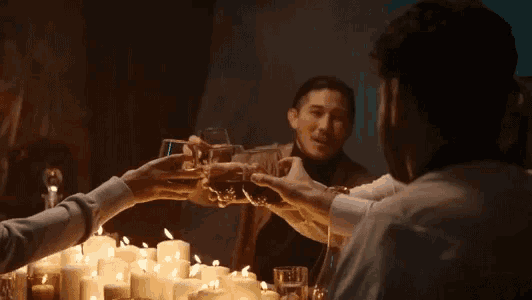 a group of people are sitting at a table with candles and toasting with glasses of alcohol .