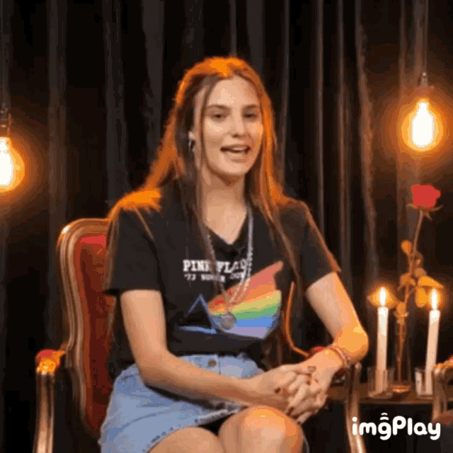 a woman wearing a pink flag t-shirt sits in a chair