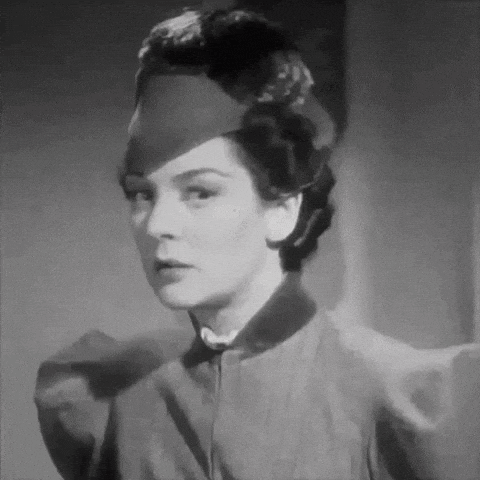 a woman wearing a hat and a jacket is looking at the camera in a black and white photo .