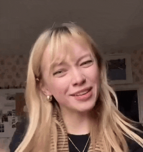a woman with blonde hair is making a funny face while wearing earrings and a scarf .