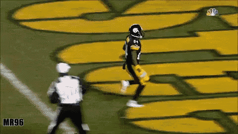 a football player is running on a field with a referee in front of a large yellow sign that says mr96