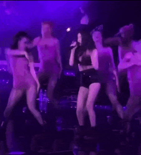 a group of women are dancing on a stage in front of a microphone in a dark room .
