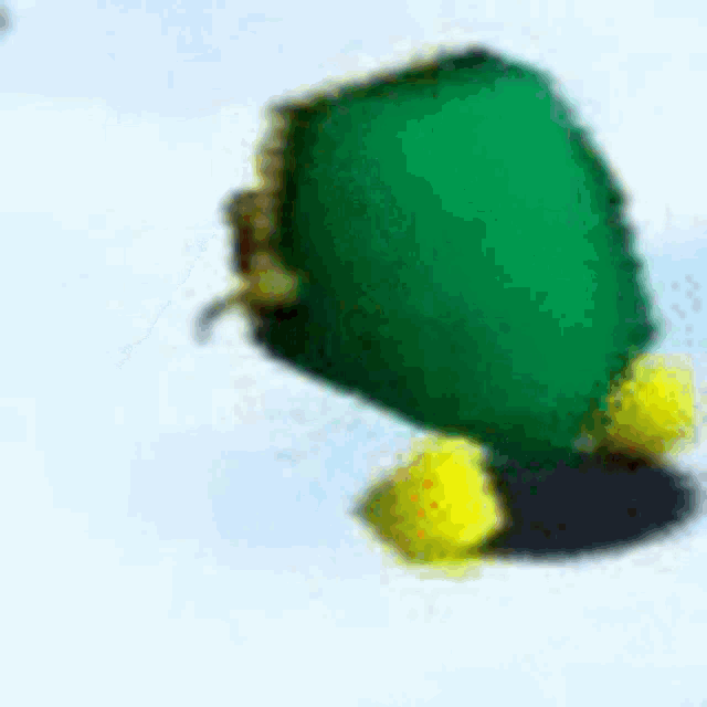a green stuffed animal with yellow feet is standing on a snowy surface .