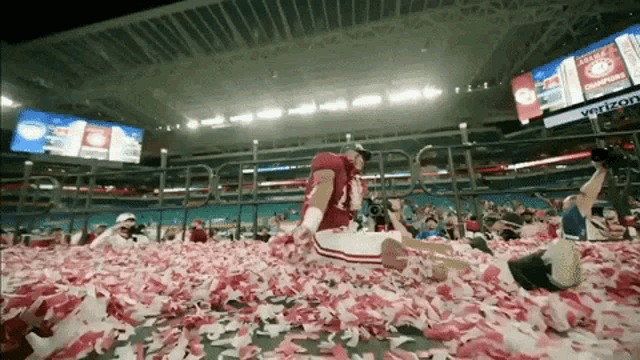 a man in a red jersey is kneeling in a pile of confetti in a stadium sponsored by verizon