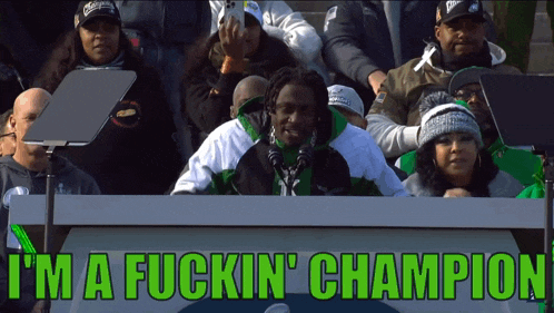 a man in a green jacket stands in front of a sign that says i 'm a fuckin ' champion