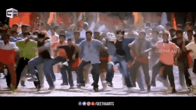 a group of people are dancing in front of a sign that says ' geetha arts ' on it .