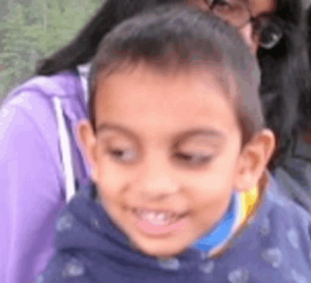 a close up of a child 's face with a woman in a purple shirt behind him