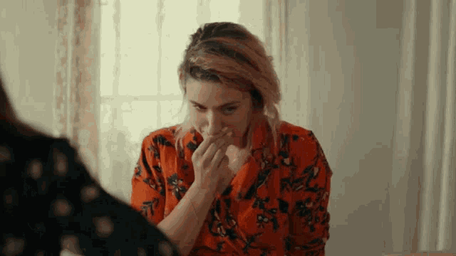 a woman in an orange floral shirt is covering her mouth with her hand .