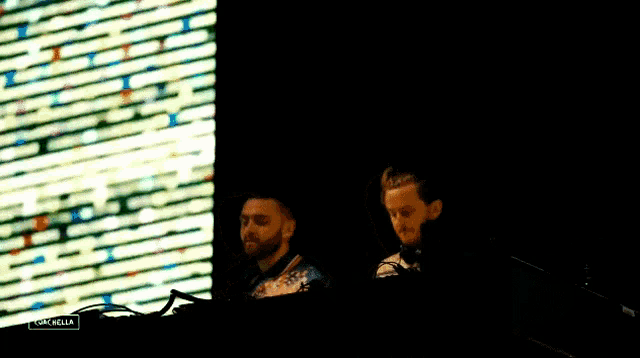 a man and a woman are sitting at a table in front of a large screen .