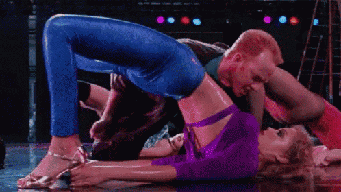 a man and a woman are dancing together on a stage . the woman is wearing a purple top and blue jeans .