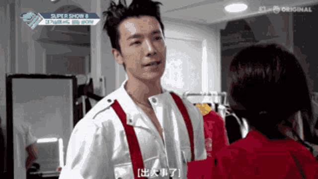 a man in a white shirt and red suspenders is talking to a woman in a room with a sign that says super show 8