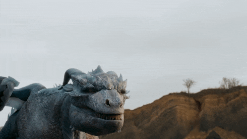 a statue of a dragon is standing on a hill with a tree in the background