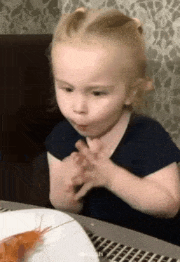 a little girl is sitting at a table with a plate of food and eating shrimp .