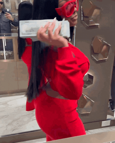 a woman in a red dress is holding a stack of money in front of a mirror