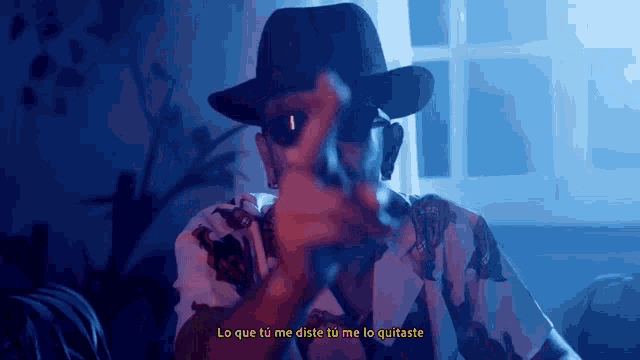 a man wearing a hat and sunglasses is smoking a cigarette with the words lo que tu me diste tu me lo quitaste above him