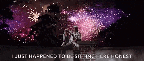 a man is sitting on top of a brick wall watching fireworks .