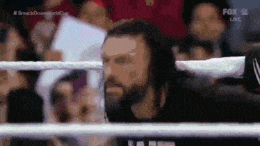 a man with a beard is standing in a wrestling ring with a crowd watching .