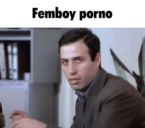 a man in a suit is sitting at a table with a plant in the background and the words femboy porno written above him .