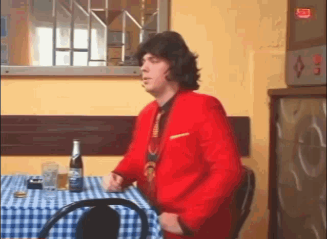 a man in a red suit is sitting at a table with a bottle of beer on it