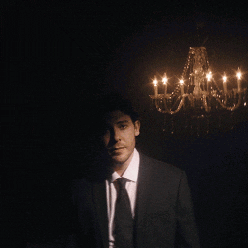 a man in a suit and tie is adjusting his jacket in front of a chandelier