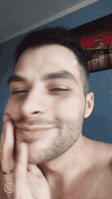 a man without a shirt is smiling and touching his face with his hand