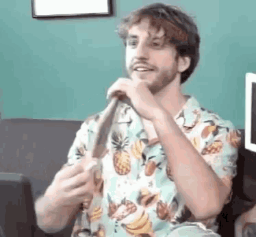 a man with a beard is sitting on a couch holding a banana in his hand .